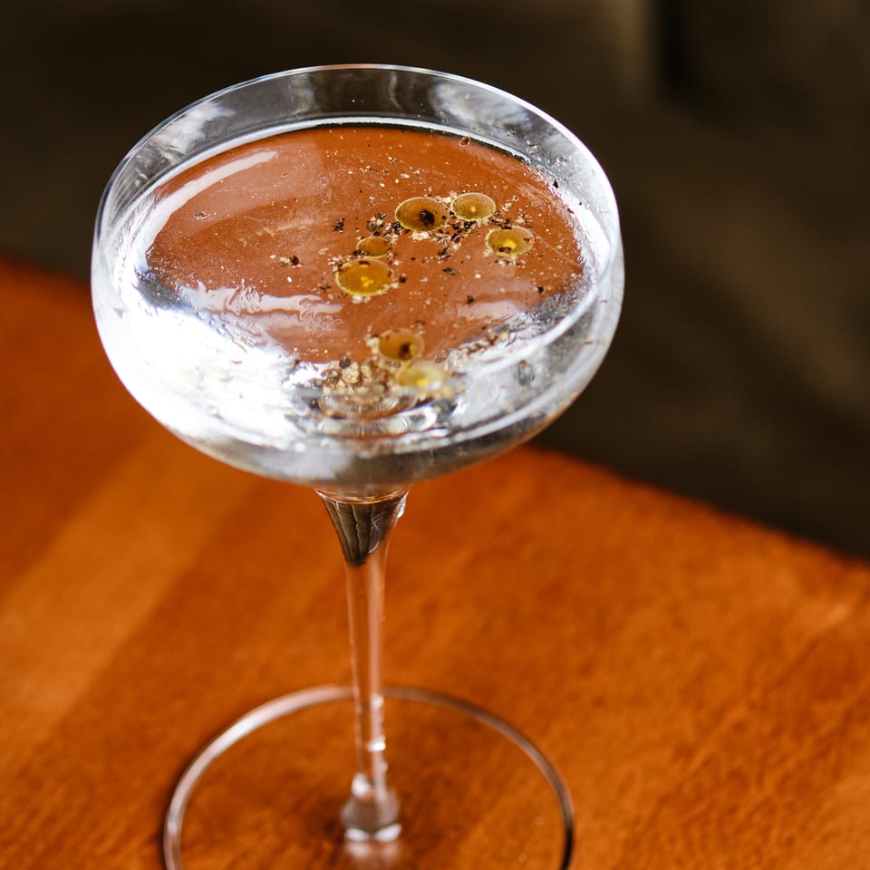 Close-up of a pink cocktail in a stemmed glass, garnished with citrus slices and spices on a wooden table.
