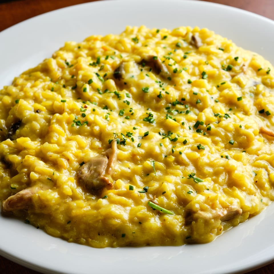 Creamy golden mushroom risotto garnished with chopped chives, served on a white plate atop a wooden table.